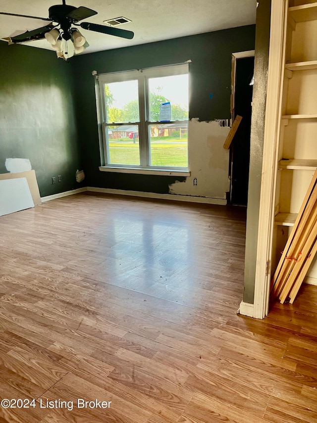 empty room with built in shelves, ceiling fan, and wood-type flooring