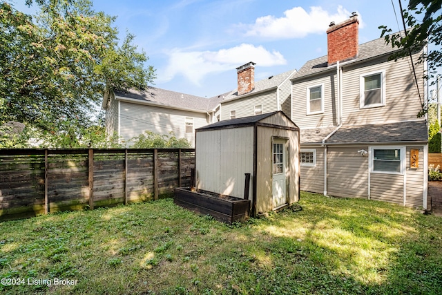 rear view of house featuring an outbuilding, a fenced backyard, a yard, and a storage shed