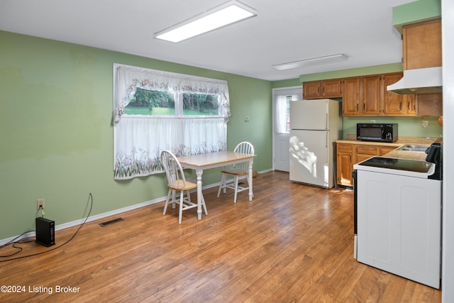 kitchen with white refrigerator, light hardwood / wood-style flooring, range, and custom exhaust hood