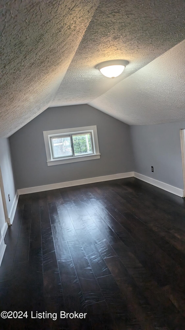 additional living space with dark wood-type flooring, vaulted ceiling, and a textured ceiling