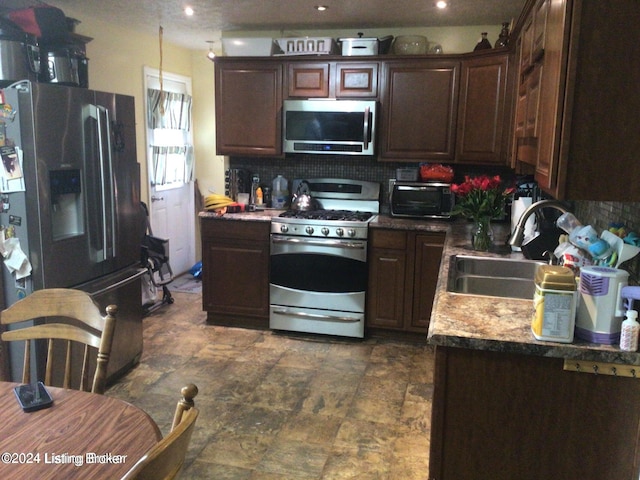 kitchen featuring dark brown cabinets, stainless steel appliances, backsplash, sink, and dark tile patterned flooring