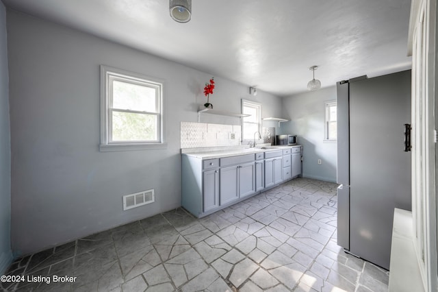 kitchen featuring stainless steel fridge, light tile patterned floors, decorative backsplash, and sink