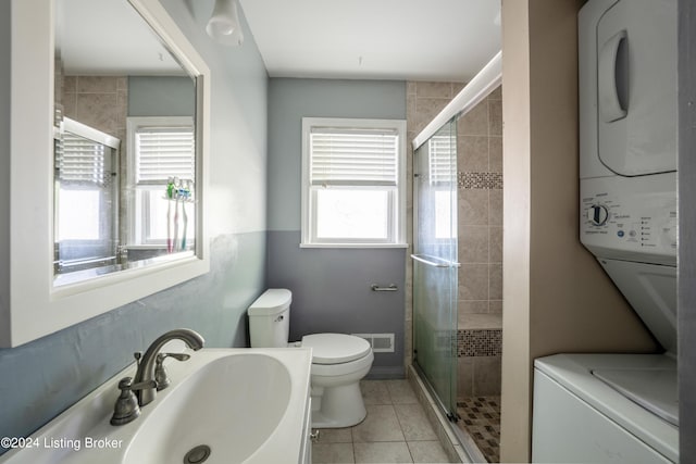 bathroom with toilet, an enclosed shower, stacked washer / drying machine, and tile patterned flooring