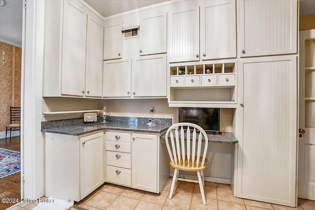 kitchen featuring white cabinetry, dark stone counters, built in desk, and light tile patterned floors