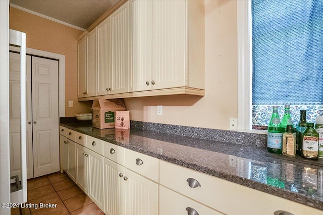 kitchen with light tile patterned flooring, ornamental molding, and dark stone countertops