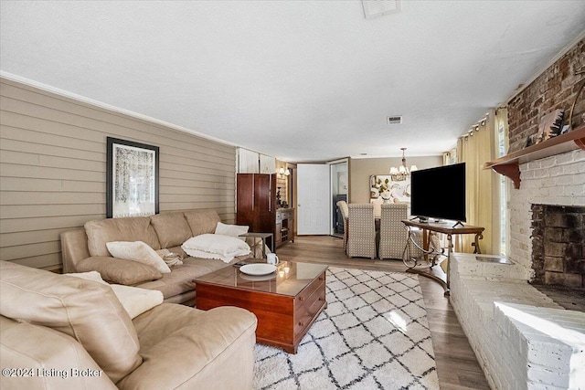 living room with a brick fireplace, a chandelier, a textured ceiling, and light hardwood / wood-style floors