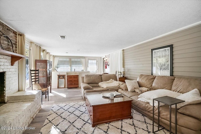 living room with a textured ceiling, a brick fireplace, and light wood-type flooring