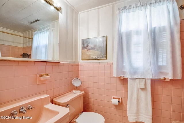 bathroom with tile walls, toilet, and a healthy amount of sunlight