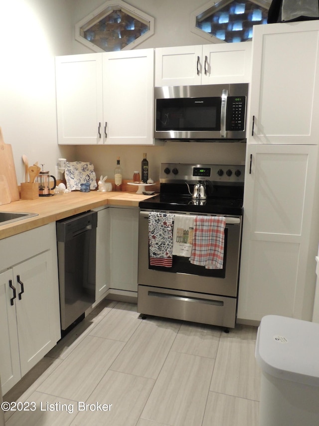 kitchen featuring light tile patterned floors, white cabinets, stainless steel appliances, and butcher block counters