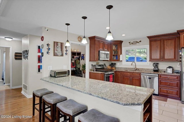 kitchen with pendant lighting, appliances with stainless steel finishes, sink, light hardwood / wood-style floors, and light stone counters