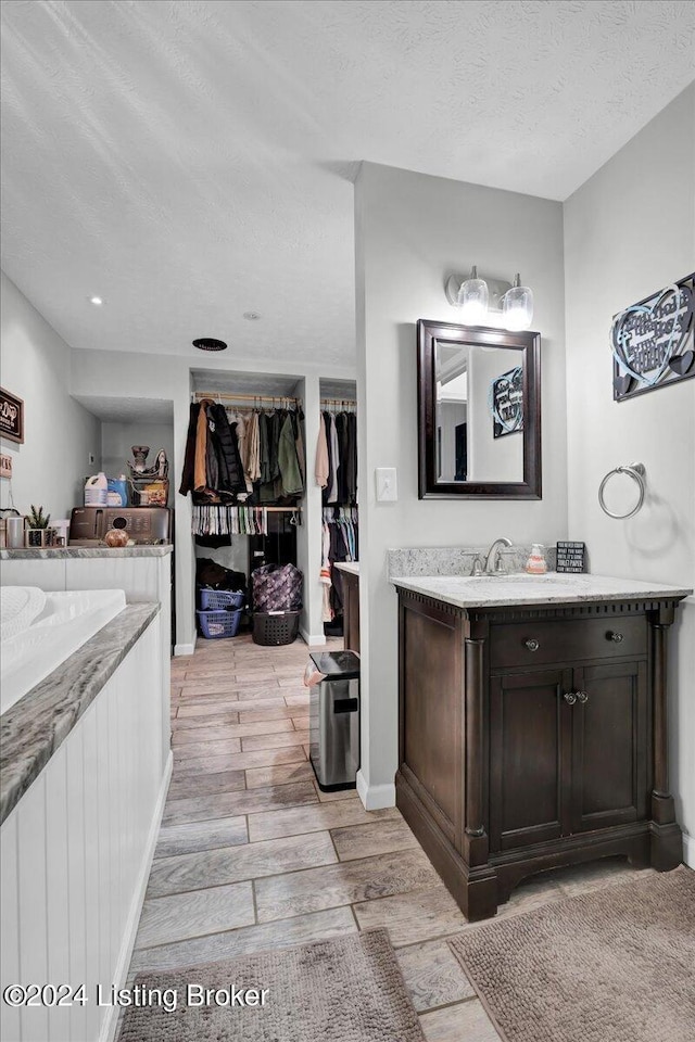 bathroom with a textured ceiling, wood-type flooring, vanity, and a bathtub