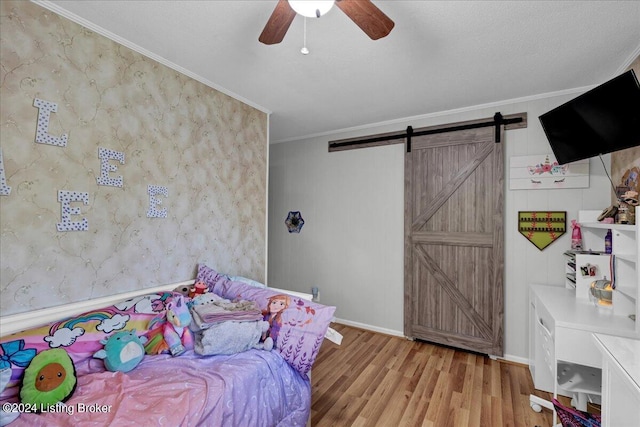 bedroom featuring a barn door, crown molding, ceiling fan, and light hardwood / wood-style floors