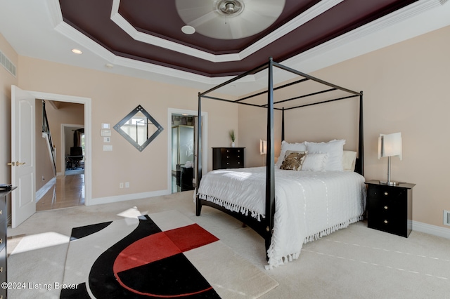 bedroom with ceiling fan, a raised ceiling, crown molding, and light colored carpet