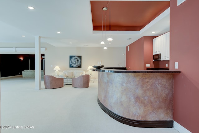 interior space featuring white cabinets, light carpet, kitchen peninsula, and a tray ceiling