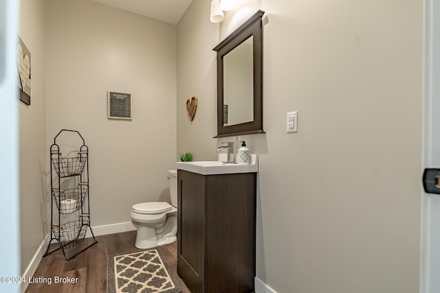 half bathroom featuring baseboards, vanity, toilet, and wood finished floors