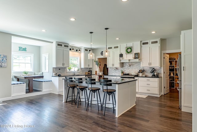 kitchen with dark countertops, a kitchen island, glass insert cabinets, a kitchen breakfast bar, and white cabinetry