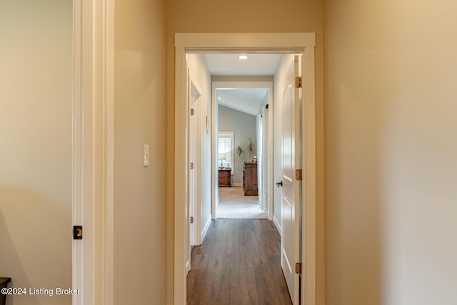 hall featuring lofted ceiling, baseboards, and dark wood-style flooring