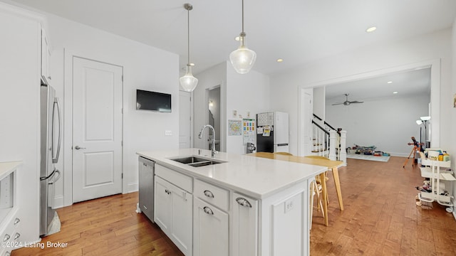 kitchen with white cabinets, hanging light fixtures, light hardwood / wood-style floors, sink, and a center island with sink