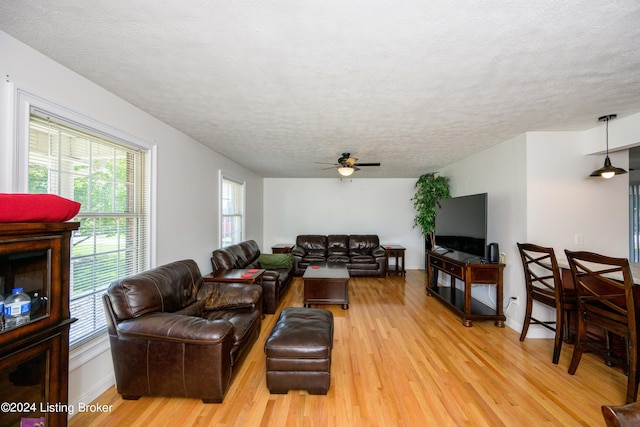 living room featuring ceiling fan, light wood-type flooring, and a textured ceiling