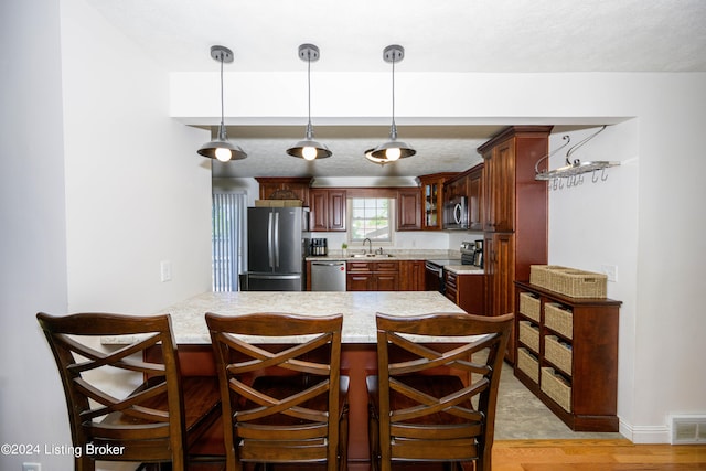 kitchen with a kitchen bar, decorative light fixtures, appliances with stainless steel finishes, light hardwood / wood-style flooring, and kitchen peninsula