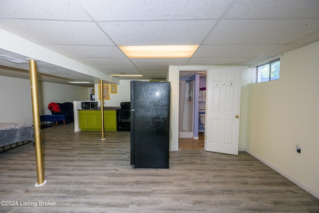 basement with a drop ceiling, light hardwood / wood-style floors, and black fridge