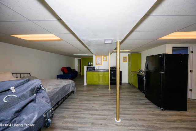 bedroom featuring a drop ceiling, wood-type flooring, and black fridge