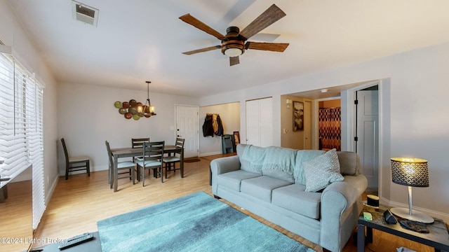 living room featuring ceiling fan with notable chandelier and light hardwood / wood-style flooring