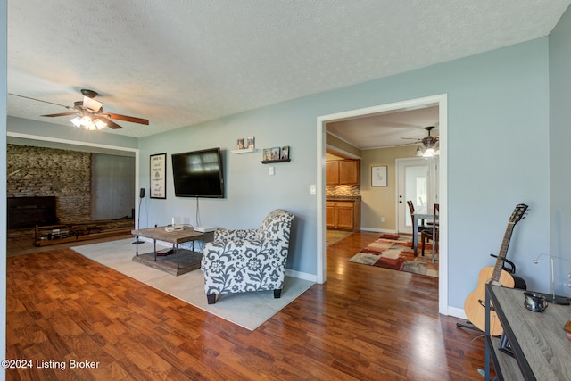 living room featuring hardwood / wood-style flooring, a fireplace, a textured ceiling, and ceiling fan