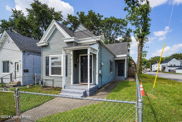 shotgun-style home featuring a shingled roof, a front yard, and fence