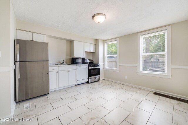 kitchen with light tile patterned floors, sink, appliances with stainless steel finishes, a textured ceiling, and white cabinetry