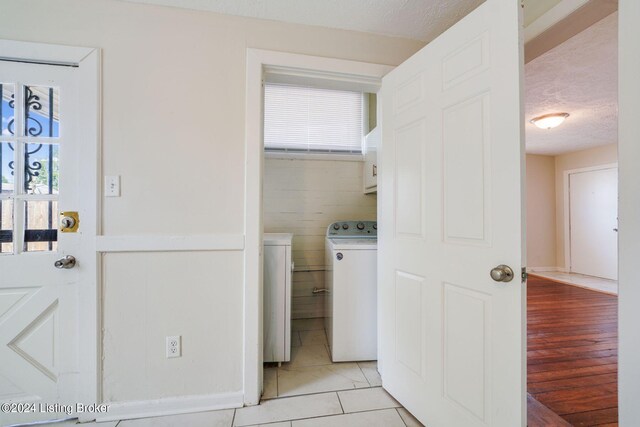 clothes washing area featuring a textured ceiling, light hardwood / wood-style flooring, cabinets, and washing machine and clothes dryer