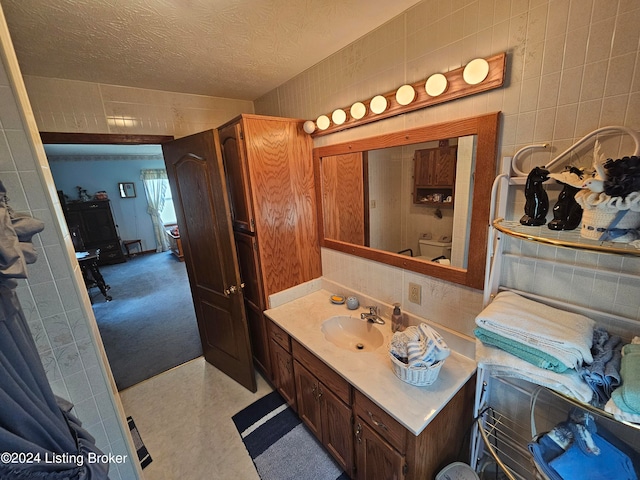 bathroom with a textured ceiling, vanity, toilet, and tile walls