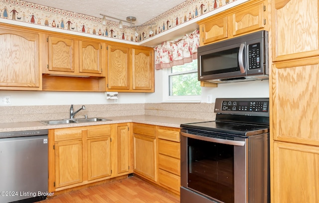 kitchen featuring sink, stainless steel appliances, a textured ceiling, and light hardwood / wood-style flooring