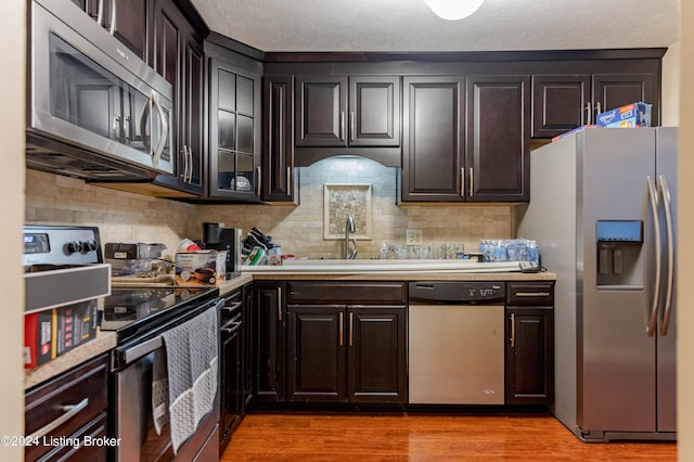 kitchen featuring dark brown cabinetry, decorative backsplash, light hardwood / wood-style flooring, and stainless steel appliances