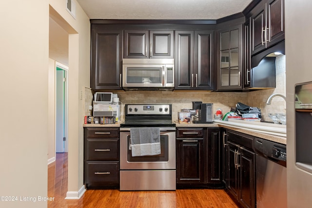 kitchen with dark brown cabinets, stainless steel appliances, and light wood-type flooring