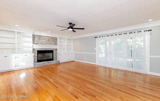 unfurnished living room with crown molding, a brick fireplace, built in features, light wood-type flooring, and ceiling fan