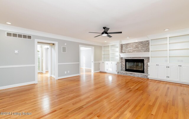 unfurnished living room featuring ceiling fan, a brick fireplace, light hardwood / wood-style flooring, built in features, and crown molding