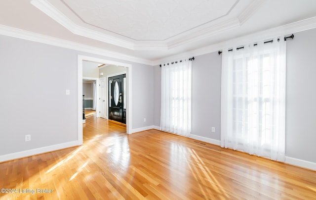 empty room with a tray ceiling, crown molding, baseboards, and wood finished floors