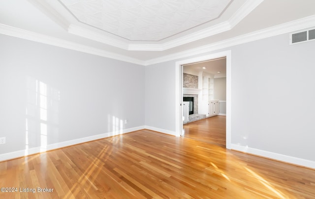 unfurnished room with a large fireplace, wood finished floors, visible vents, baseboards, and ornamental molding