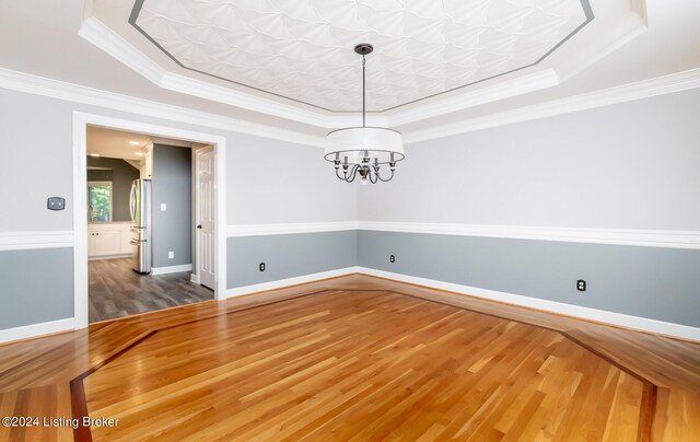 unfurnished dining area with crown molding, hardwood / wood-style flooring, an inviting chandelier, and a raised ceiling