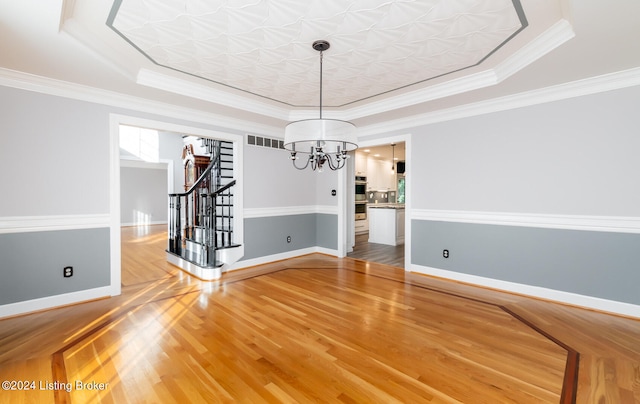 unfurnished dining area with crown molding, wood-type flooring, and a raised ceiling