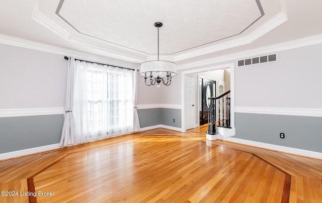 unfurnished dining area with crown molding, hardwood / wood-style floors, a chandelier, and a tray ceiling