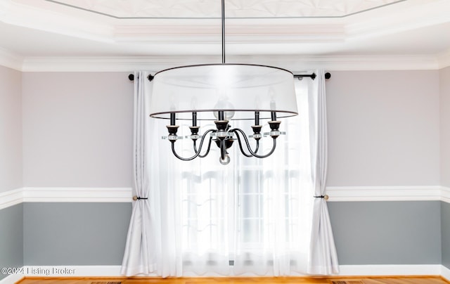 interior details featuring a chandelier, a raised ceiling, and crown molding