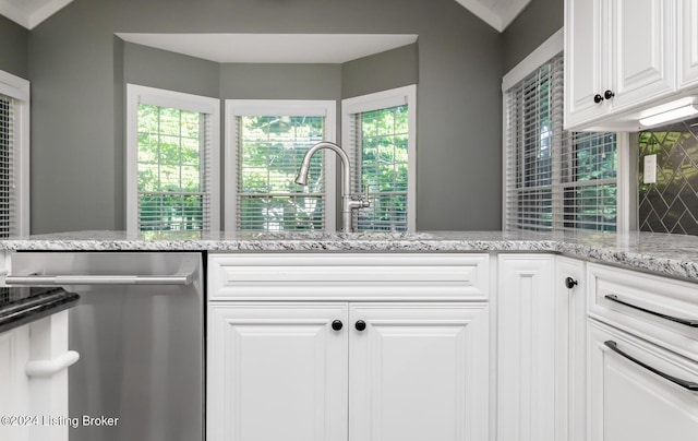 kitchen featuring decorative backsplash, white cabinets, dishwasher, light stone countertops, and a sink