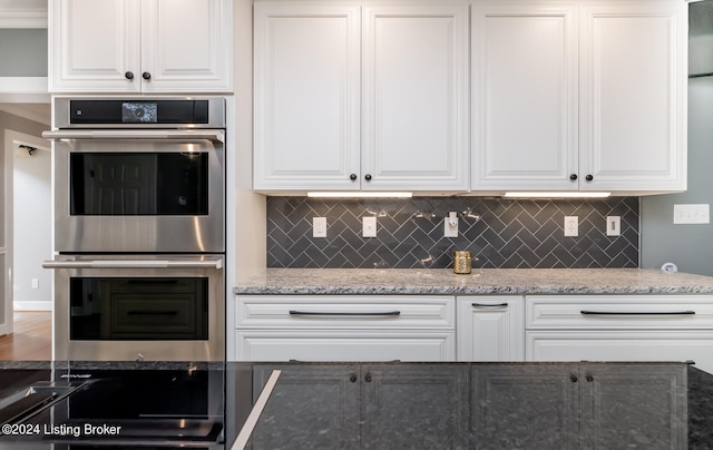 kitchen featuring stainless steel double oven, white cabinets, light stone counters, and tasteful backsplash