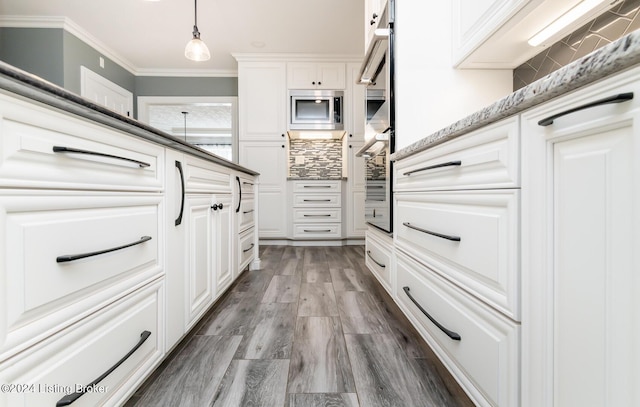 kitchen featuring wood finished floors, white cabinetry, decorative backsplash, stainless steel microwave, and crown molding