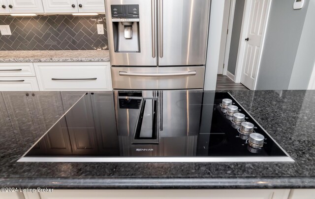 kitchen with stainless steel fridge, white cabinets, backsplash, and dark stone counters