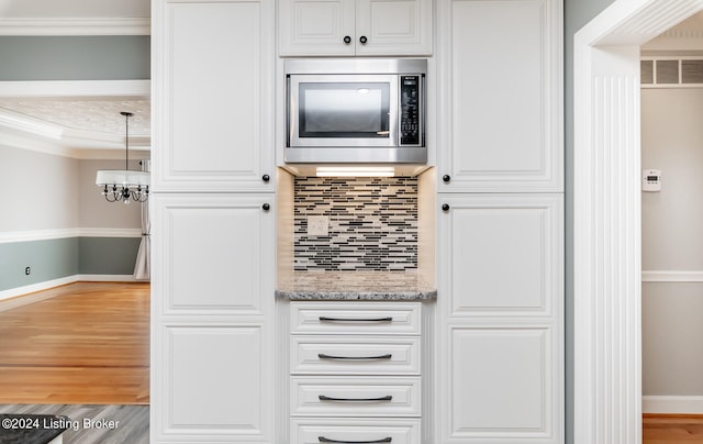 interior space featuring an inviting chandelier, stainless steel microwave, light stone countertops, light wood-type flooring, and decorative light fixtures