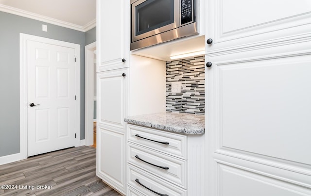 kitchen with light wood finished floors, decorative backsplash, stainless steel microwave, ornamental molding, and white cabinetry