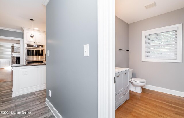 bathroom with vanity, crown molding, wood-type flooring, and toilet